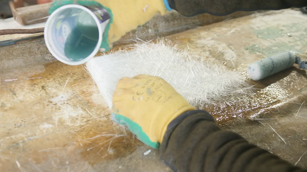 Pouring and rolling polyester resin over fiberglass boat repair