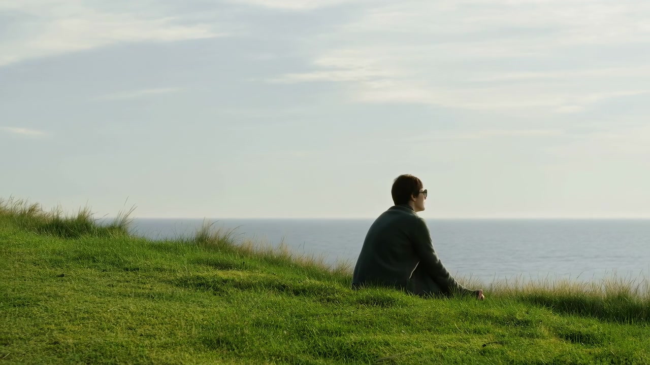 Person sitting on grass relaxing or observing the surroundings, in outdoor open field with green grass and sky, with grass, sky, with grass, clothing dark texture, with green, blue accents.
