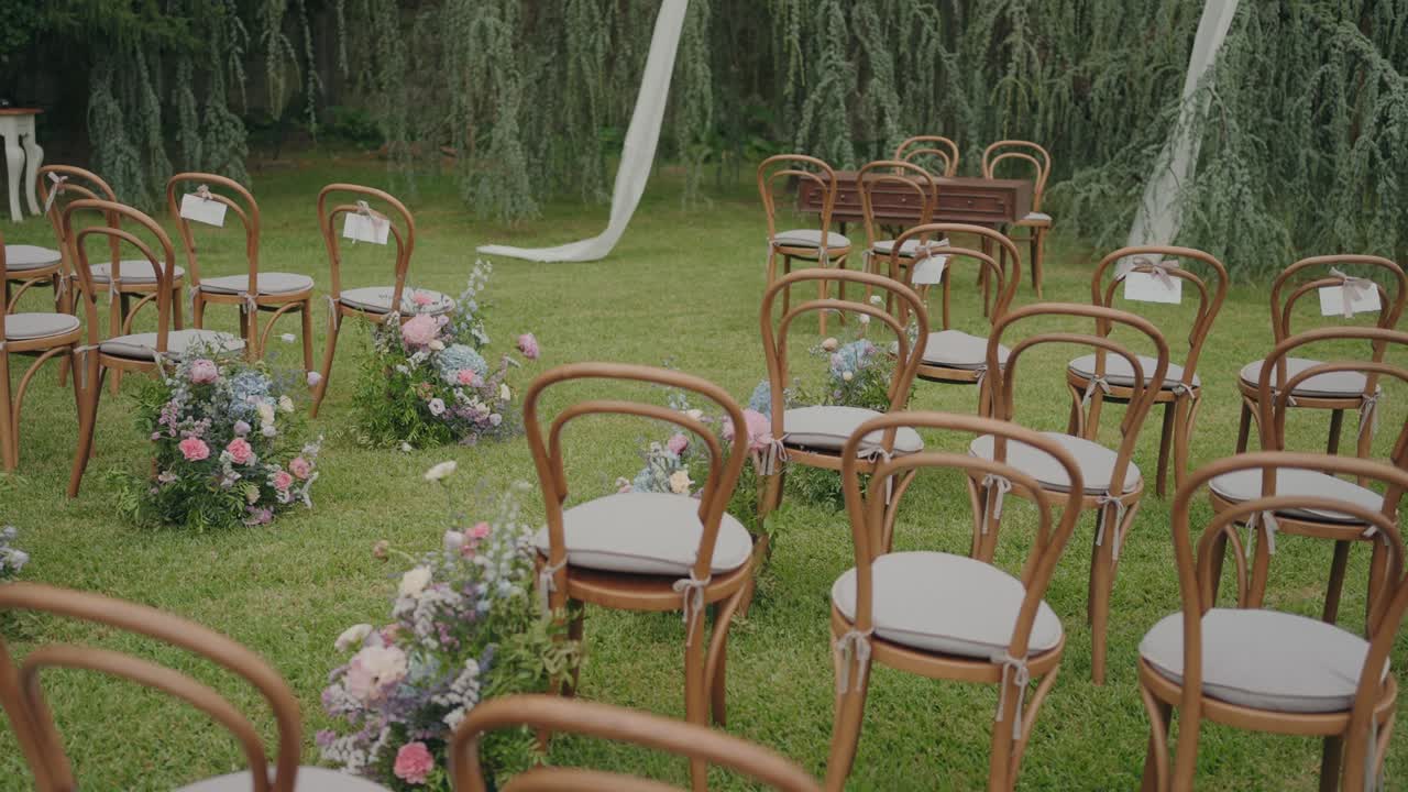 Serene garden setup of wooden chairs adorned with pastel blooms for a romantic ceremony