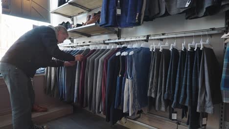 Man-in-store-looking-through-a-range-of-tartan-jackets,-waistcoats-and-trousers