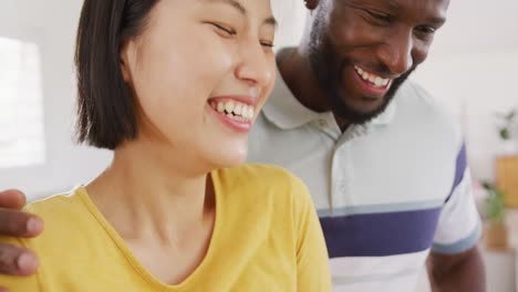 Happy-diverse-couple-cooking,-embracing-and-talking-in-kitchen