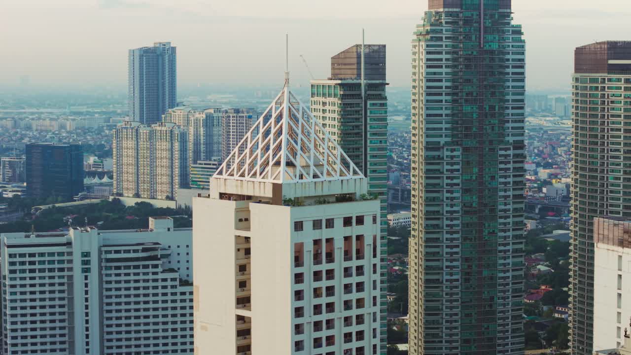 Torre geométrica branca se destaca entre arranha-céus cinza-azulados, Manila, Filipinas.