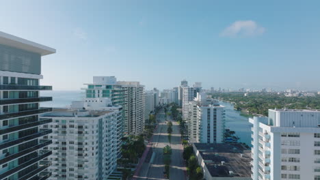 Forwards-fly-above-road-between-tall-modern-buildings.-Luxury-apartments-or-hotels-on-sea-coast.-Miami,-USA