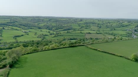 aerial over a plateau ridge to reveal a valley of gorgeous english countryside, fields, trees, and rural homesteads