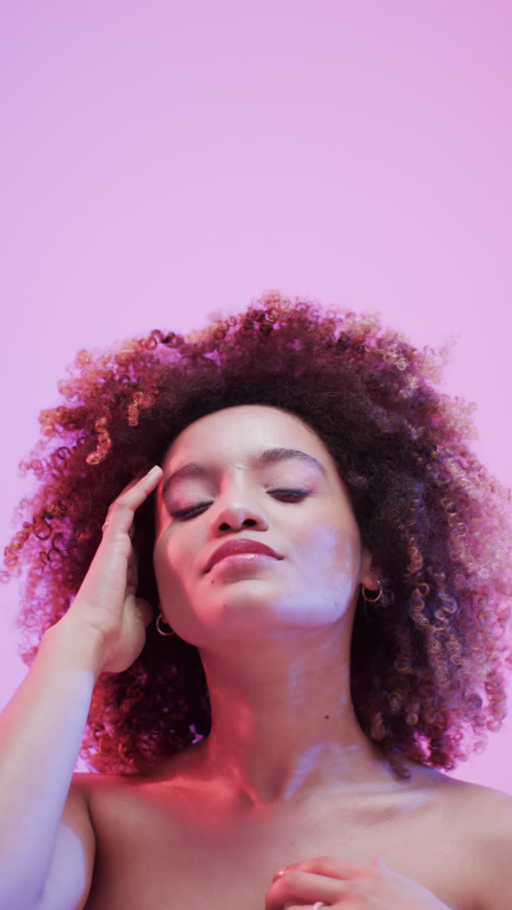 Vertical video of biracial woman with dark hair in blue and pink light with copy space, slow motion