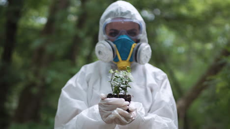 scientist in protective gear holding a small plant