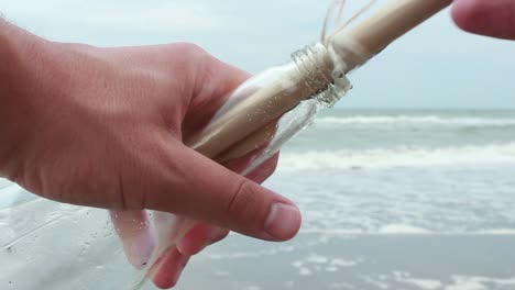 joven abriendo un mensaje en una botella en una playa de arena 1