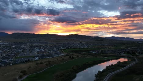 a brilliant sunset over a suburban community reflecting off a river - aerial flyover