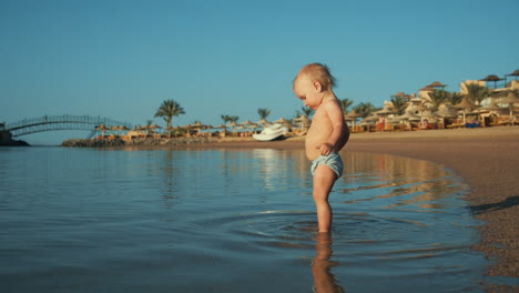 Entzückendes-Kleinkind,-Das-Im-Sommerurlaub-Wasser-Im-Warmen-Meer-Am-Sandstrand-Spritzt.