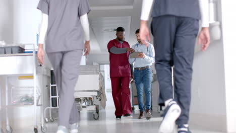 diverse male doctors discussing work using tablet walking in hospital corridor, slow motion