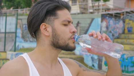 handsome guy drinking fresh water from a plastic bottle in a skate park