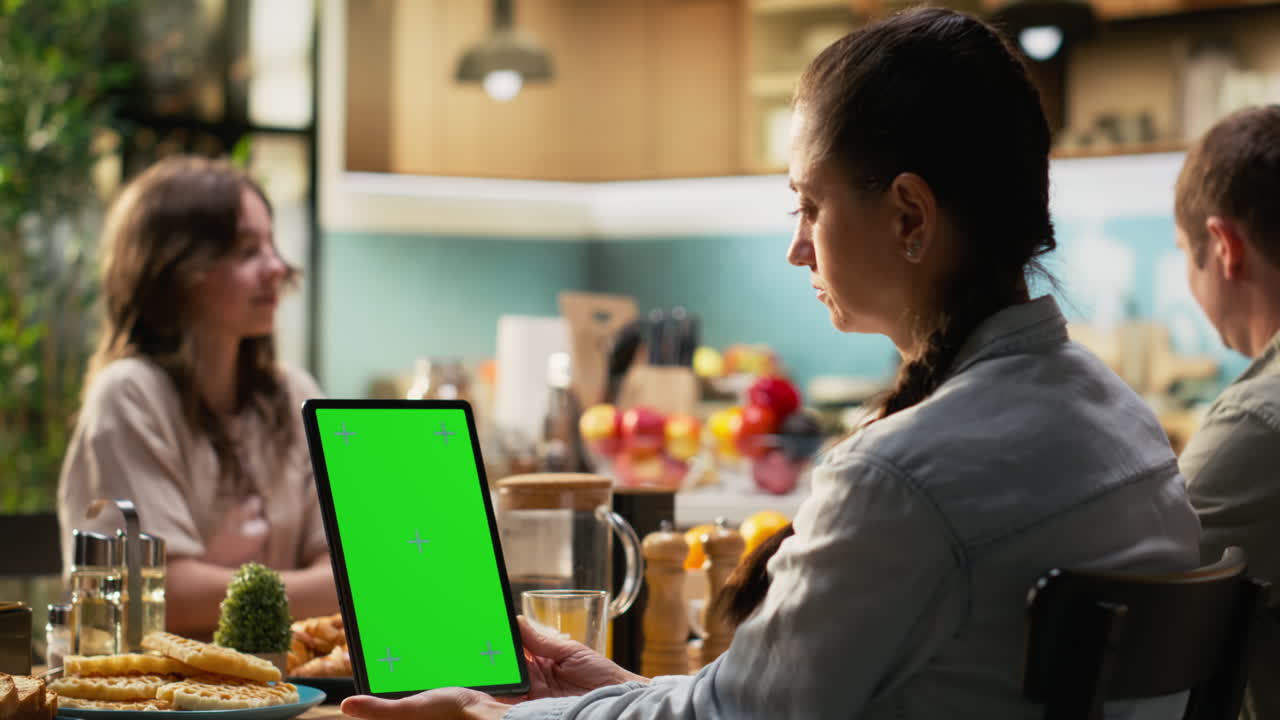 Vertical green screen on tablet next to family sharing breakfast in home kitchen