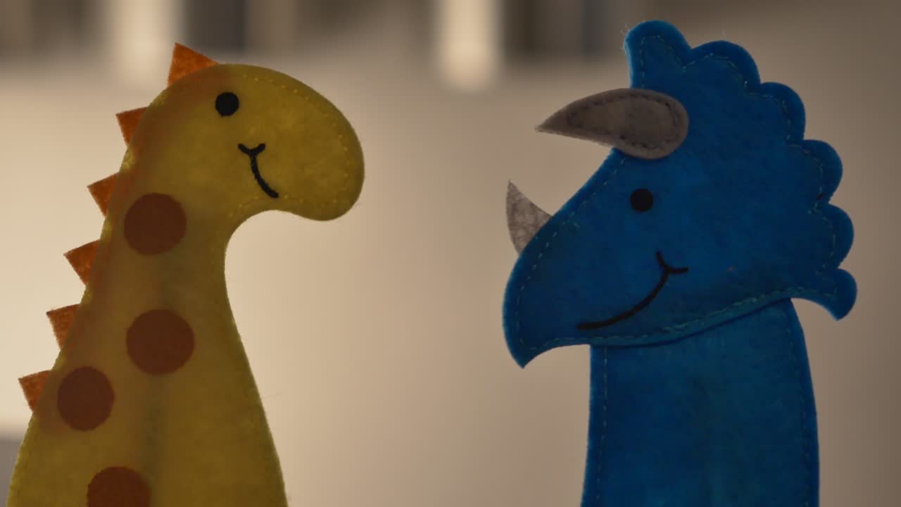 A blue triceratops and a yellow stegosaurus finger puppet talk together