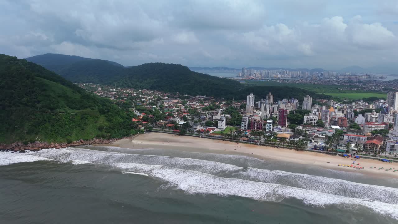 Praia do Tombo -ranta aaltojen ja kaupungin siluetin kera Guarujassa, São Paulossa, Brasiliassa, ilmapanorointi takaisin.