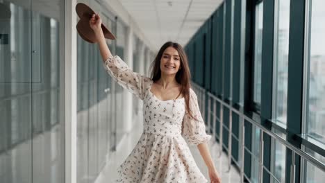 Happy-young-woman-walking-down-the-hall-in-a-board-and-hat