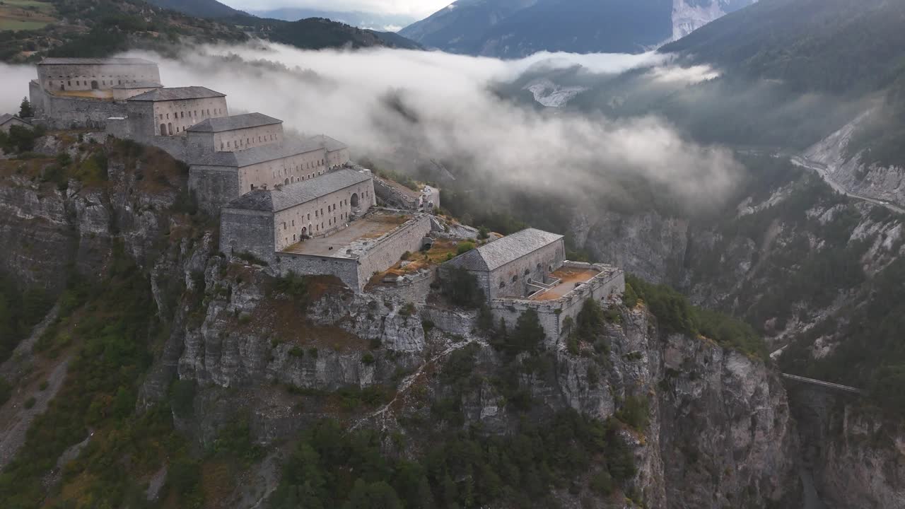 Drone si allontana in retromarcia da un antico castello in alta montagna circondato dalle nuvole in 4K
