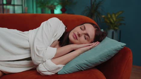 tired young woman lying down in bed taking a rest at home, napping, falling asleep on orange couch