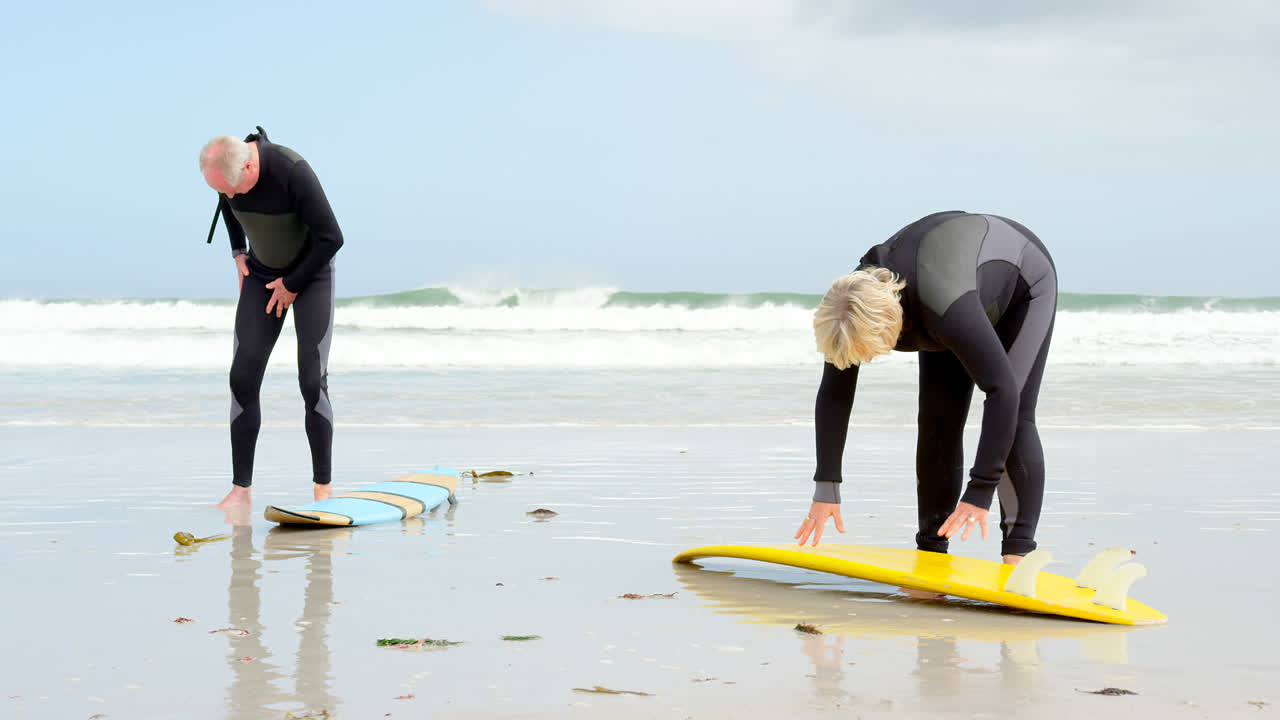 vista frontal de una vieja pareja caucásica atando la correa de la tabla de surf en la playa 4k
