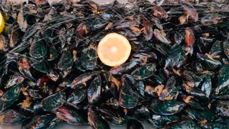 Pile-of-fresh-mussels-on-display-with-fruit,-sprayed-with-water,-close-up-pullback