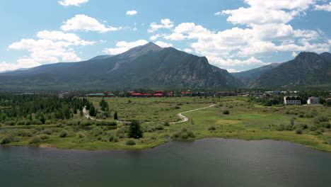 aerial shot zooming across lake dillon to reveal a busy paved trail full of cyclists and joggers in colorado's rocky mountains