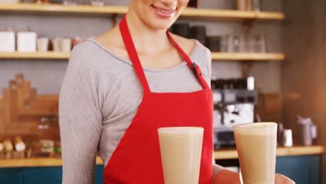 Smiling-waitress-carrying-two-cold-coffees-in-cafe