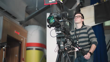 camera operator adjusting high-end broadcast camera on tripod in studio, focusing on equipment, preparing for shooting scene in professional tv production setup with studio lights