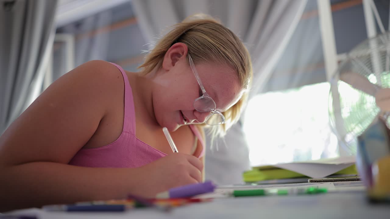 Primo piano di una giovane ragazza che studia i compiti di scuola al tavolo in una casa luminosa.