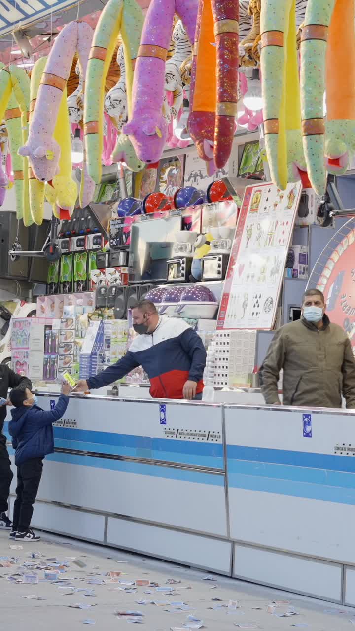 A colorful game stall with plush toy prizes and people at a carnival