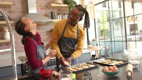 happy diverse couple in aprons decorating christmas cookies in kitchen, copy space, slow motion