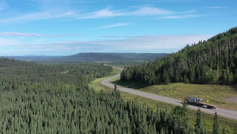 drone flies over winding alaska highway through lush boreal forest