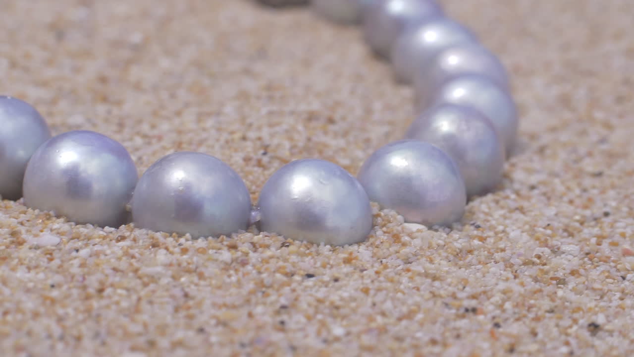 primer plano cinematográfico de un collar de perlas naturales de plata con joyas de plata en una playa de arena, 120 fps, slomo