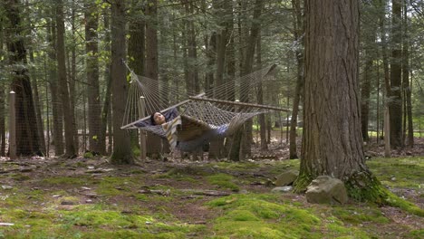 young adult female swinging in hammock between woodland trees relaxing and carefree life