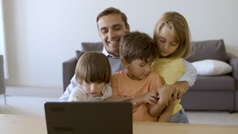 Padre-Amoroso-Abrazando-A-Los-Niños-Y-Mirando-La-Pantalla-Del-Portátil.