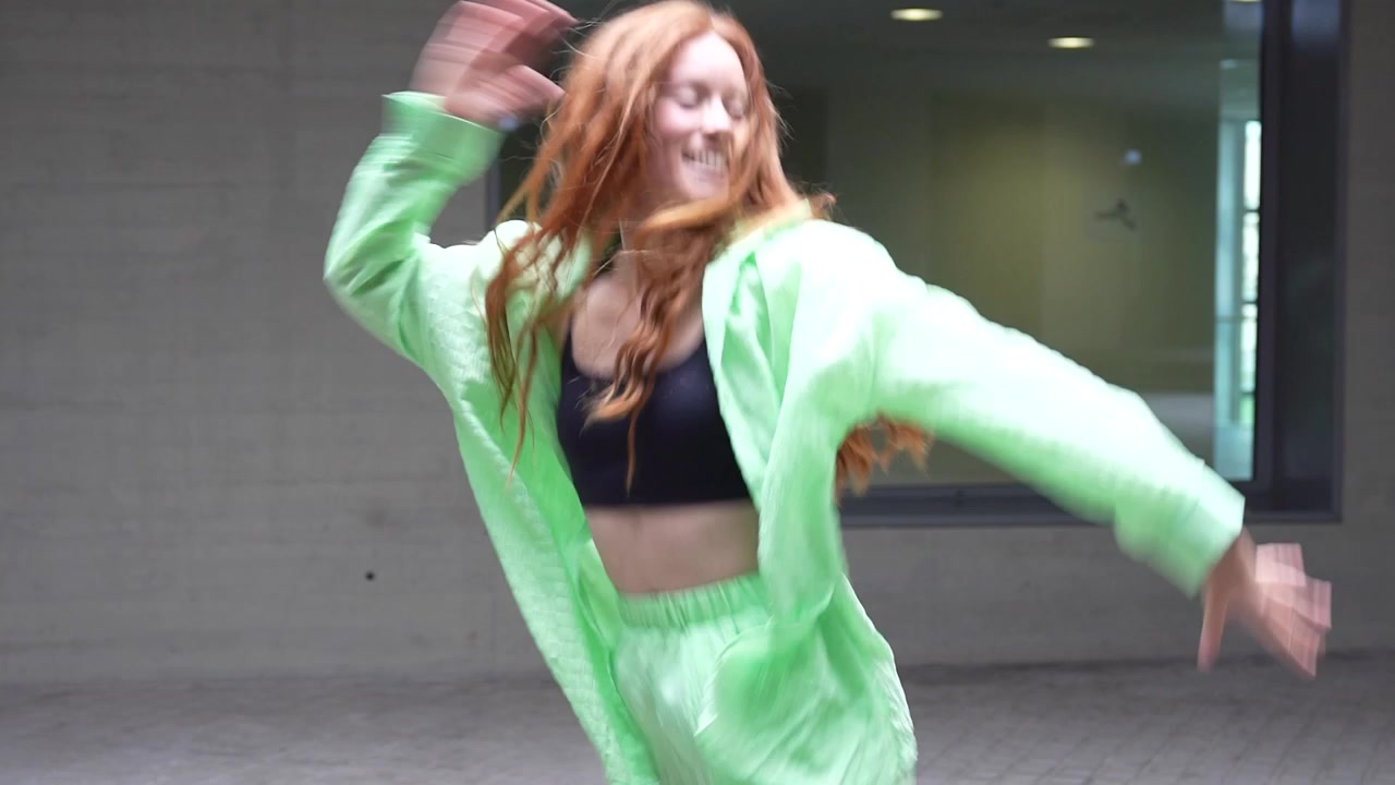 An exuberant woman in a vibrant green ensemble is dancing energetically outdoors