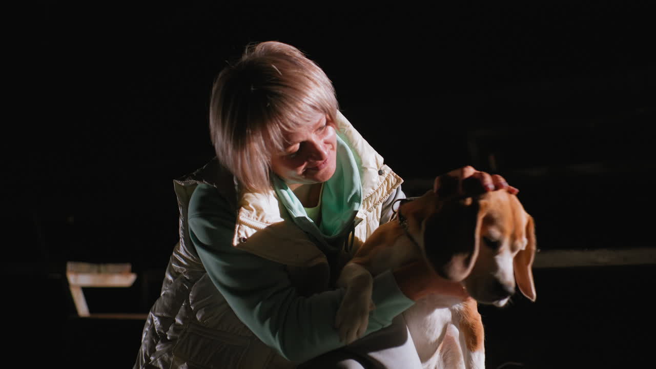 Dog owner hugging her pet passionately under soft lighting during peaceful night moment showcasing emotional connection, warmth, and trust between human and dog in quiet stadium setting