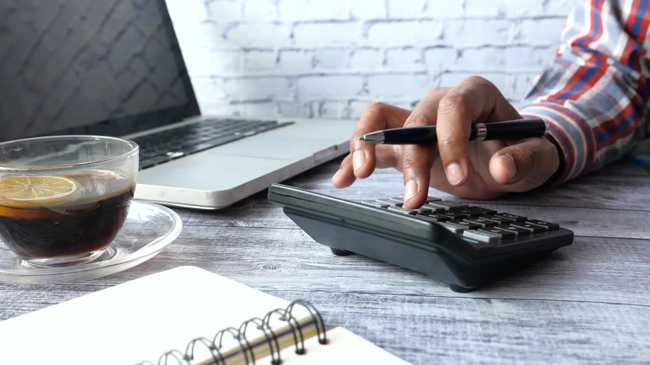 Person using a calculator and laptop at a desk