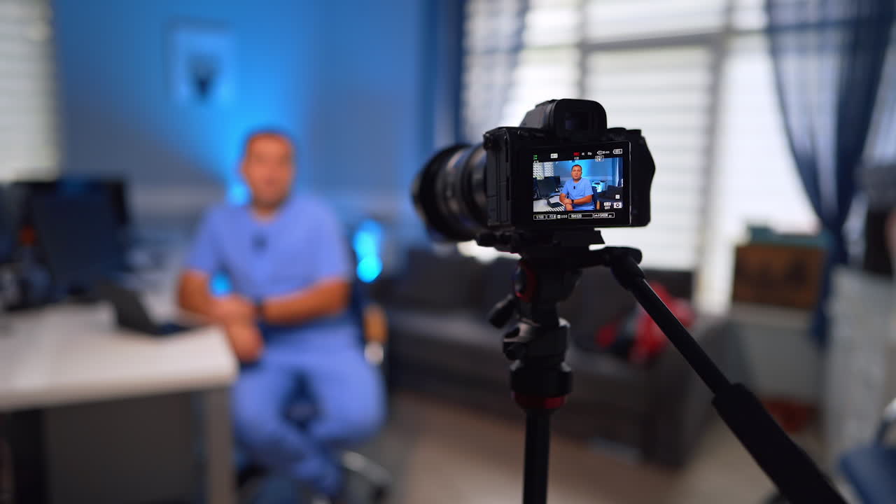 Modern professional camera set in front of the man sitting at desk. Selective focus on a doctor recording video vlog