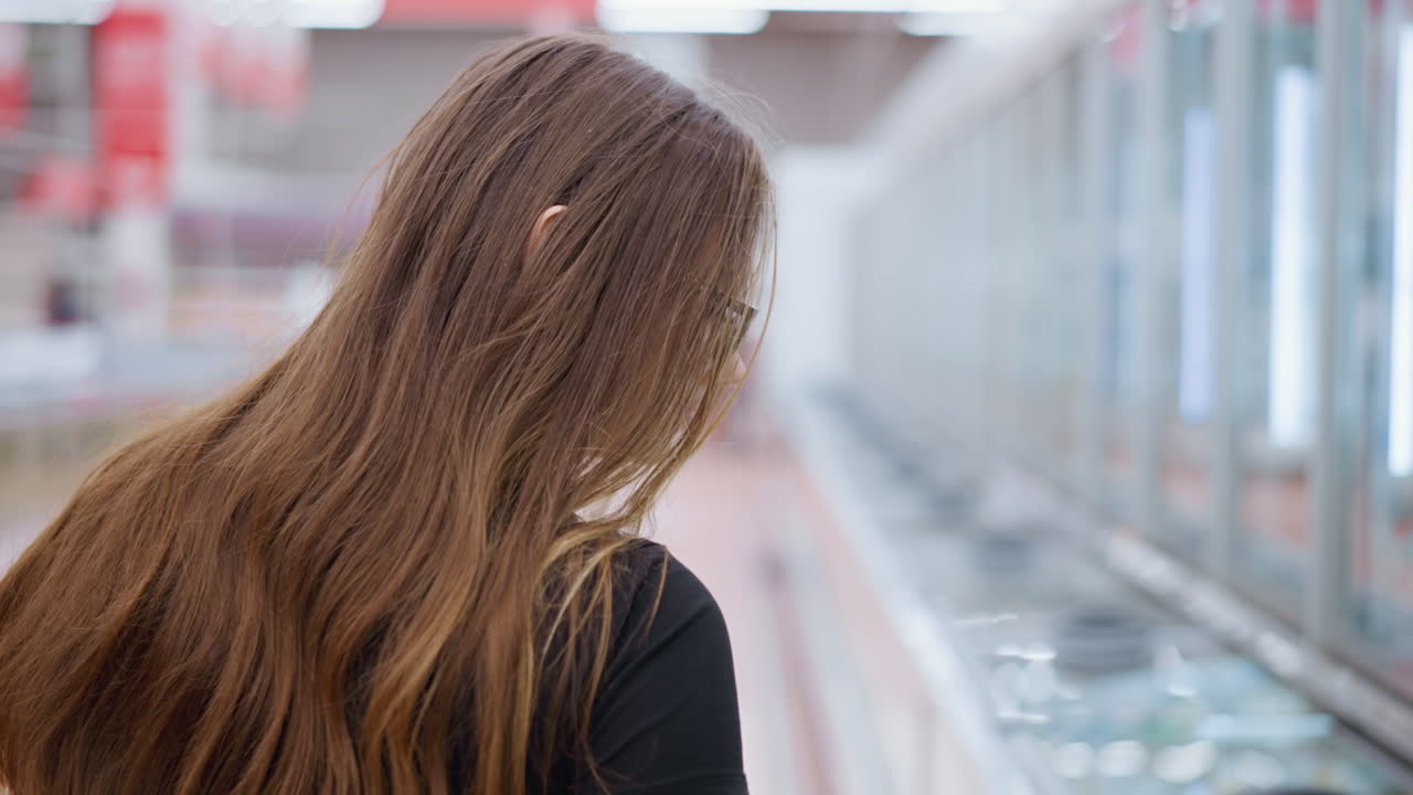 쇼핑몰에서 디스플레이를 보고 있는 젊은 여성, 유리창에 반사되고 다른 쇼핑객들이 배경에서 보이는 내용물을 확인하기 위해 가까이 다가오고 있습니다.