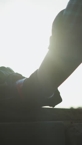 primer plano de alguien con camisa a cuadros y guante protector, con los rayos del sol iluminando la mano derecha