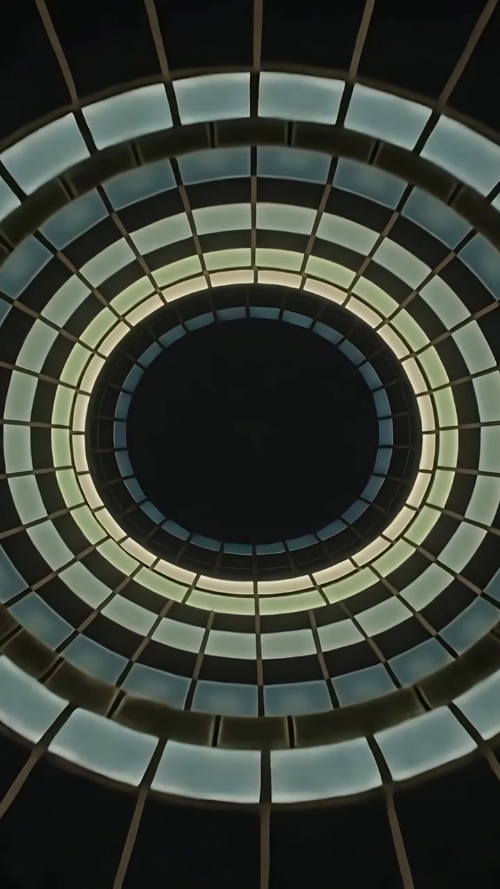 Vertical video: Rotating camera revealing oculus shifting lit rings at atrium, mullions, dark core