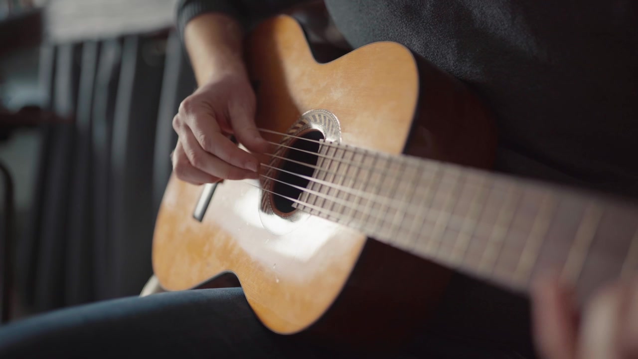 Una persona che strimpella una chitarra acustica al chiuso con luce naturale e un'atmosfera accogliente.