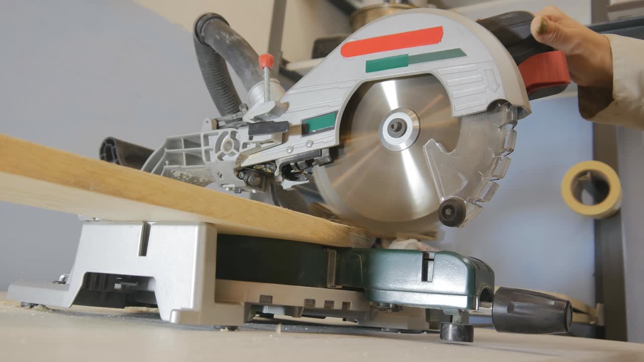 una mujer carpintero corta una parte de una tabla con una sierra de mitra. baja la sierra circular con la mano y hace el trabajo. a la mujer le encanta trabajar con madera. 4k