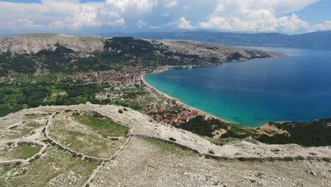 aerial fly over a mountain revealing a small coastal town of baška, krk, croatia