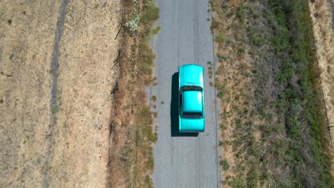 Drone-footage-of-light-blue-classic-mustant-driving-down-rural-country-roads-in-California,-during-the-day