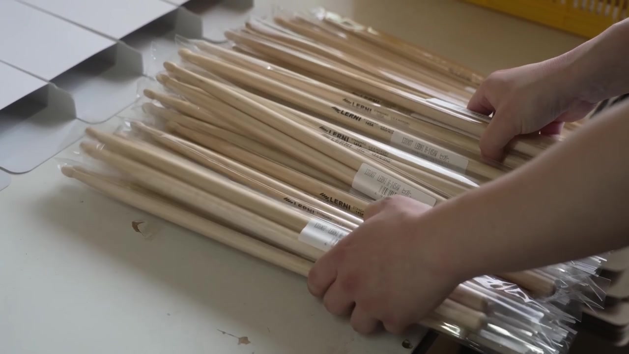 Mani di operaio che imballano paia di bacchette sigillate in pellicola termoretraibile in scatole di cartone bianche per la spedizione in fabbrica.