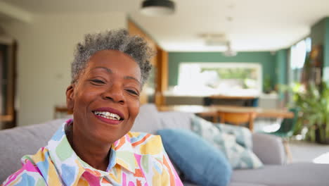 Retrato-De-Una-Mujer-Mayor-Sonriente-Relajándose-En-El-Sofá-De-Su-Casa-En-El-Salón-Comedor