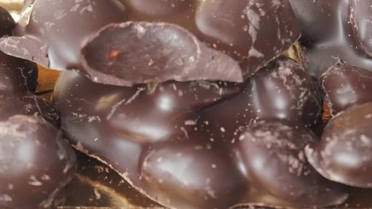 Close-up pan right view of glossy dark chocolate almonds arranged on a golden tray
