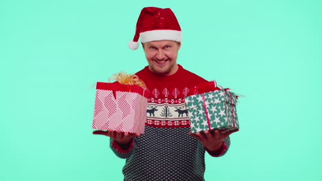 Man-wears-red-New-Year-presenting-Christmas-gift-boxes,-stretches-out-his-hands-to-camera-smiling