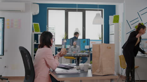 Entrepreneur-woman-sitting-at-desk-in-company-office-eating-sandwich-during-online-videocall-conference