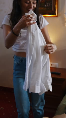 suitcase with clothes on bed in a hotel. happy woman unpacking luggage. joyful girl unpacks her clothes and dances happily during vacation. vertical video